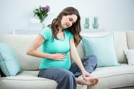 a pregnant woman sitting on a couch touching her stomach and foot